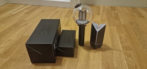 Reviewer's unboxed BTS Official Light Stick Ver.4 and cradle, shown with the black packaging on a wooden floor.