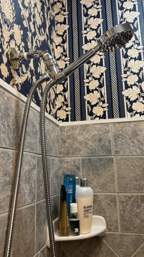 Customer's handheld shower head set installed with an extension arm in a shower with tiled and wallpapered walls.