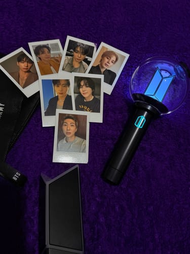 Reviewer's BTS Official Light Stick Ver.4 lit up in blue, shown with its cradle and instant photos on a purple surface.