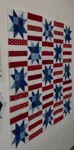 Customer's finished Red, White, and Cute quilt top on a wall, showing the blue star and red stripe design.