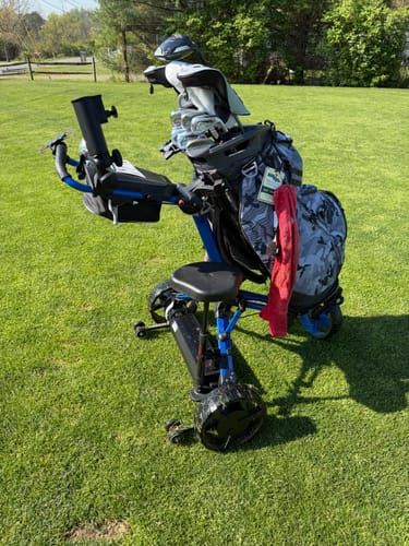Customer's Club Booster V2Pro installed on a blue push cart with a seat and golf bag, sitting on a green fairway.