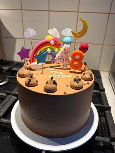Customer's Classic Chocolate Cake with custom toppers, including a rainbow, stars, and number candles for '4' and '8'.