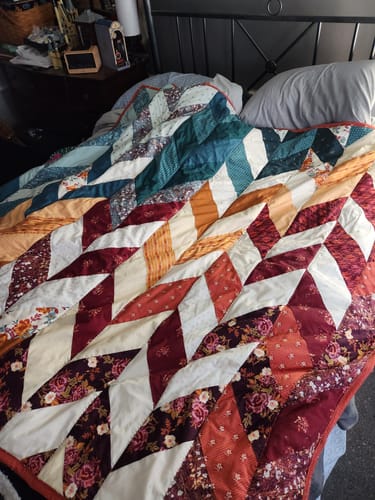 Customer's finished Herringbone Ombre quilt kit, showing the colorful herringbone pattern on a bed.