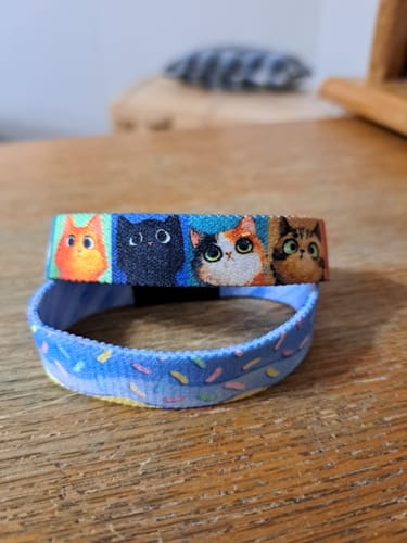 Customer's blue Happy Birthday Bracelet with sprinkles shown below a colorful cat bracelet on a wooden table.