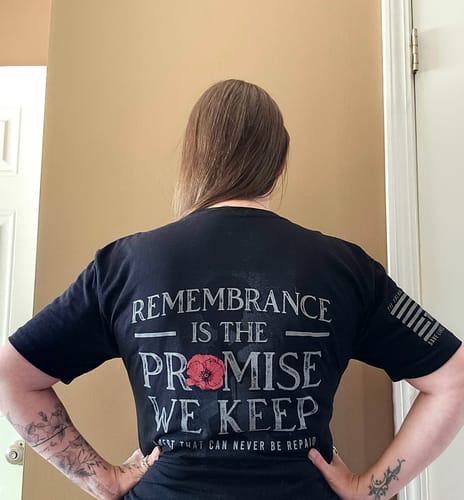 Reviewer from behind wearing the black The Promise We Keep tee, showing the 'Remembrance' graphic with a red poppy.