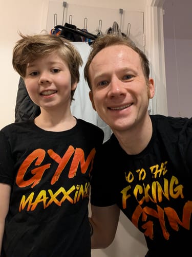 Customer's son wearing the black Gymmaxxing Kids T-Shirt, posing happily with an adult in a similar shirt.