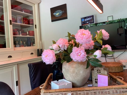 Klant toont de volle, roze Zijden Pioenrozen in een rustieke vaas op tafel.