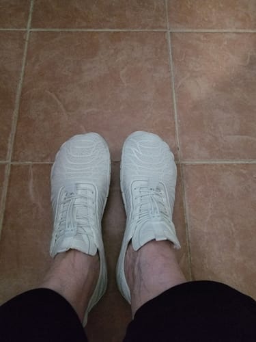 A customer's view looking down at their white Lorax Pro barefoot shoes on a tile floor.