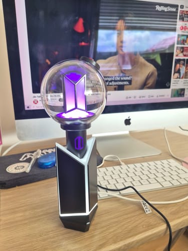 Reviewer's BTS Official Light Stick Ver.4 glowing purple while resting in its cradle on a desk.