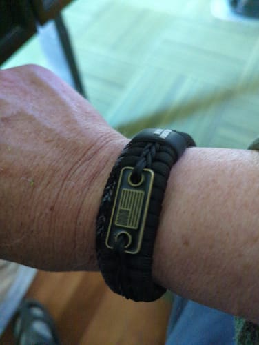 Customer's wrist showing the black Band of Brothers Paracord Bracelet with its bronze American flag emblem.