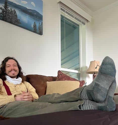 Reviewer relaxing on a couch with feet up, wearing the thick Charcoal Heather Over The Calf Socks.
