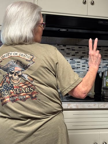 Reviewer's wife wearing the back of the military green Liberty Or Death tee and making a peace sign.