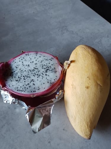 Kunde zeigt eine ganze Mango und eine aufgeschnittene Drachenfrucht aus der Früchtebox 'Thai Gold'.