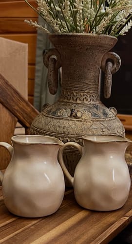 Reviewer's 2-Piece Milk Pitcher Set in Crema displayed on a rustic wooden surface in front of a decorative vase.