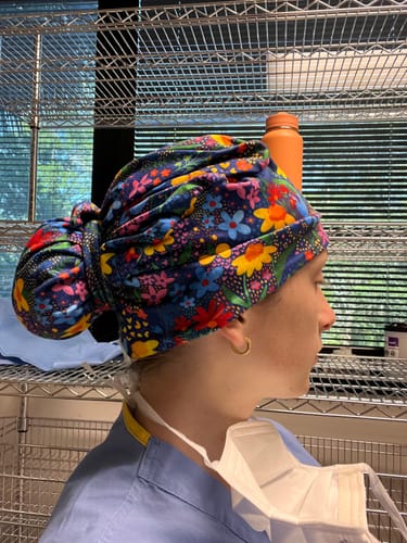 Reviewer from the side, wearing the colorful DuoStyle Scrub Hat in a ponytail style in a medical setting.