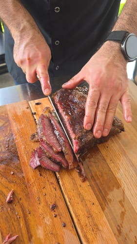 Cliente cortando un jugoso Short Rib en rebanadas sobre una tabla de madera.