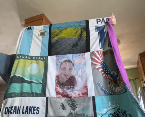 Reviewer holds up a memorial Project Repat T-Shirt Quilt made from various shirts, showing the purple fleece backing.