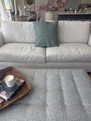 Customer's Faye in blue pillow cover centered on a light-colored sofa in a living room.