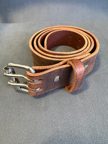 Customer's brown Legend Double Prong Retro Style belt coiled on a grey surface, showing the silver buckle.