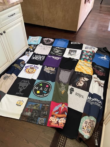 Customer's large, colorful Project Repat T-Shirt Quilt made of various t-shirts is spread out on a wooden floor.