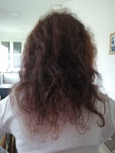 Reseñadora mostrando la parte trasera de su cabello castaño cálido y ondulado después de aplicar el Tinte 100% Natural.