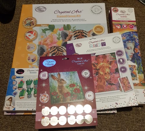 Reviewer's contents of the Crystal Art Mystery Box, showing various packaged art kits laid out together on a floor.