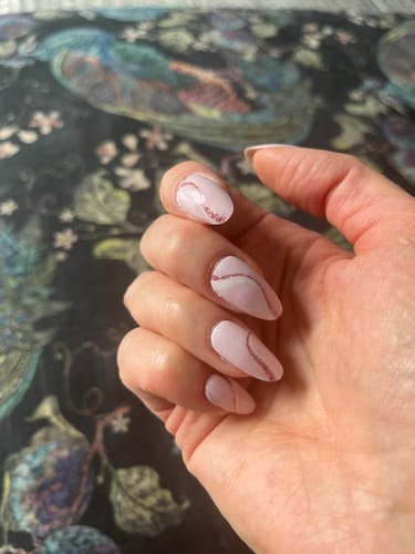 Customer's hand showing long, almond-shaped nails with the Pink Fizz gel manicure, featuring a light pink base and a glittery swirl.
