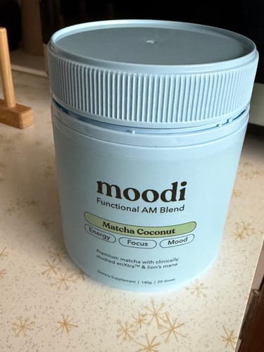 Customer's light blue tub of moodi Matcha Coconut AM blend sitting on a patterned countertop.