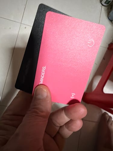 Customer holding a pink SPOTMINDERS Tracking Card in front of a black one, showing the power button icon.