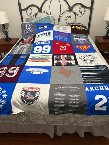 Customer's Project Repat T-Shirt Quilt made from sports jerseys and t-shirts, spread neatly on a bed.