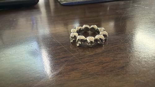 A customer's silver 10 Stages of Addiction Ring, composed of small skulls, resting on a dark wood surface.