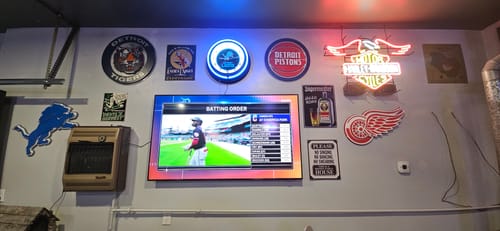 Reviewer's Detroit Red Wings wall art displayed on a wall with other Detroit sports signs and a TV.