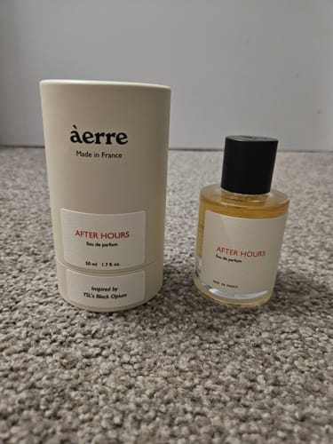Customer's After Hours perfume bottle placed next to its white cylindrical packaging on a grey carpet.