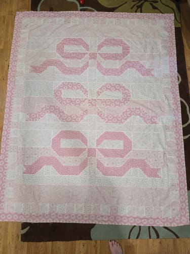 Customer's completed Love Blossoms quilt, featuring a pink and white bow pattern, laid out on a floor.
