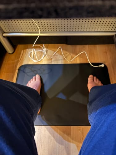Vásárló, aki a fekete EarthFlow Földeléses Szőnyegen pihenteti mezítelen lábát egy íróasztal alatt.