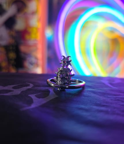 Close-up of a reviewer's Orbituary Ring, highlighting the silver skull design and red gem against colorful lights.