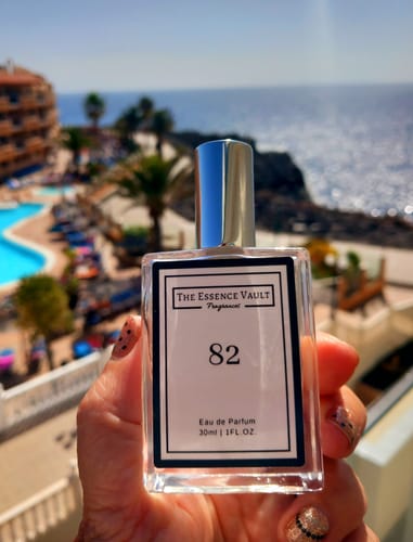Customer holding the No. 82 Mystery 30ml Perfume bottle on a sunny balcony overlooking a coastal scene.