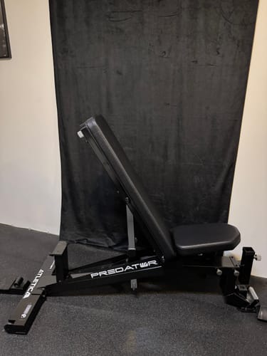 Kunde zeigt die schwarze Predator Hantelbank schräg eingestellt in seinem Homegym.