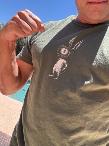 Reviewer wearing the green Programmed Perception t-shirt outdoors by a pool.