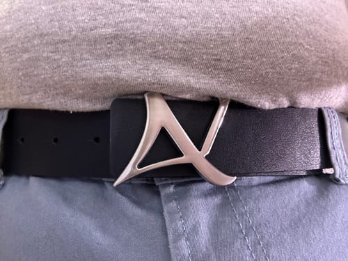 Gros plan sur la boucle-logo en métal de la ceinture réversible portée par un client.