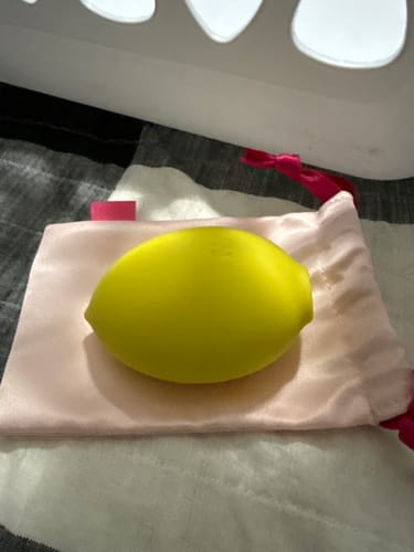 Customer's yellow, lemon-shaped Lem Clitoral Massager resting on its pink satin storage pouch.