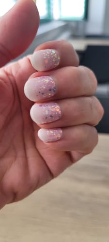 Hand einer Kundin, die die glitzernden UV-Gelfolien 'Babyboomer Princess' auf kurzen Nägeln zeigt.