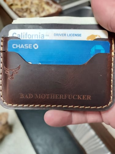 Customer holding a personalized brown leather Pflugerville Card Wallet with the phrase 'Bad Motherfucker' debossed on the front.