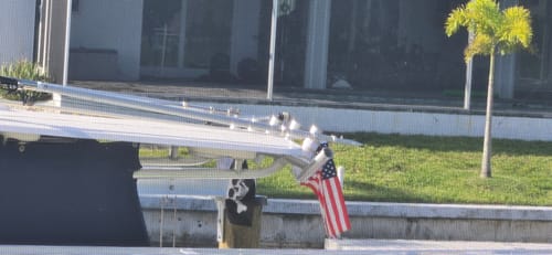 Customer's American Flag firmly attached to a silver pole holder on a boat docked near a grassy area.