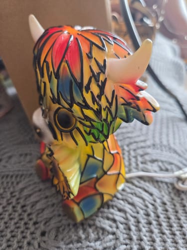 Reviewer's close-up of the multicolored Highland Cow lamp, showing a glossy, plastic-looking finish.