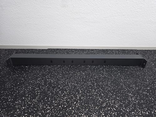 Rezensent zeigt die stabile R7 SQUAT Backtube, die auf einem gefleckten Fitnessboden liegt.