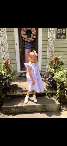 Customer's niece smiling while wearing the French Lavender Gingham Smocked Bow Dress on her graduation day.