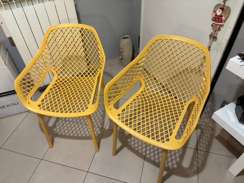 Recensore mostra le due poltrone traforate gialle in un ambiente domestico, su un pavimento piastrellato.