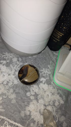 Reviewer's monthly crystal, a polished round stone with brown and beige patterns, resting on a white lace surface.