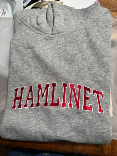 Customer's folded grey hoodie with the name 'Hamline' misspelled as 'Hamlinet' embroidered in red.